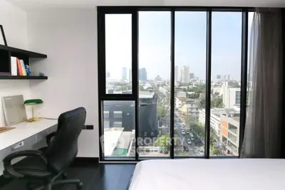 Modern bedroom with stunning city view through large windows, featuring a sleek desk and comfortable chair.