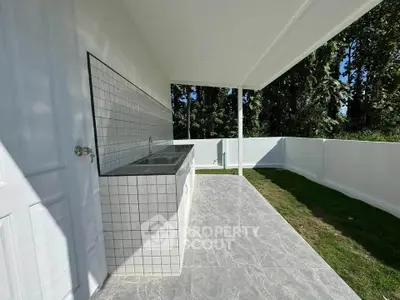Spacious outdoor balcony with tiled flooring and built-in sink, surrounded by lush greenery.