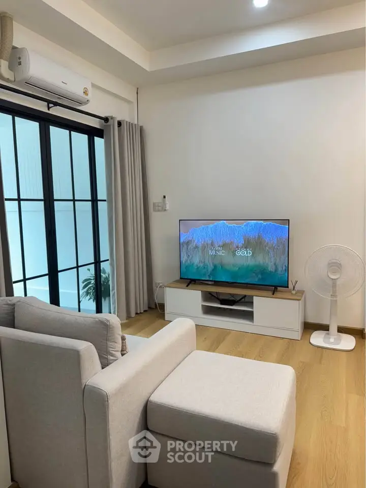 Modern living room with cozy seating and large TV, featuring sleek sliding glass doors and elegant decor.
