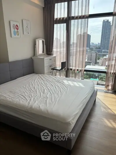 Spacious bedroom with large windows offering stunning city views in a modern apartment.