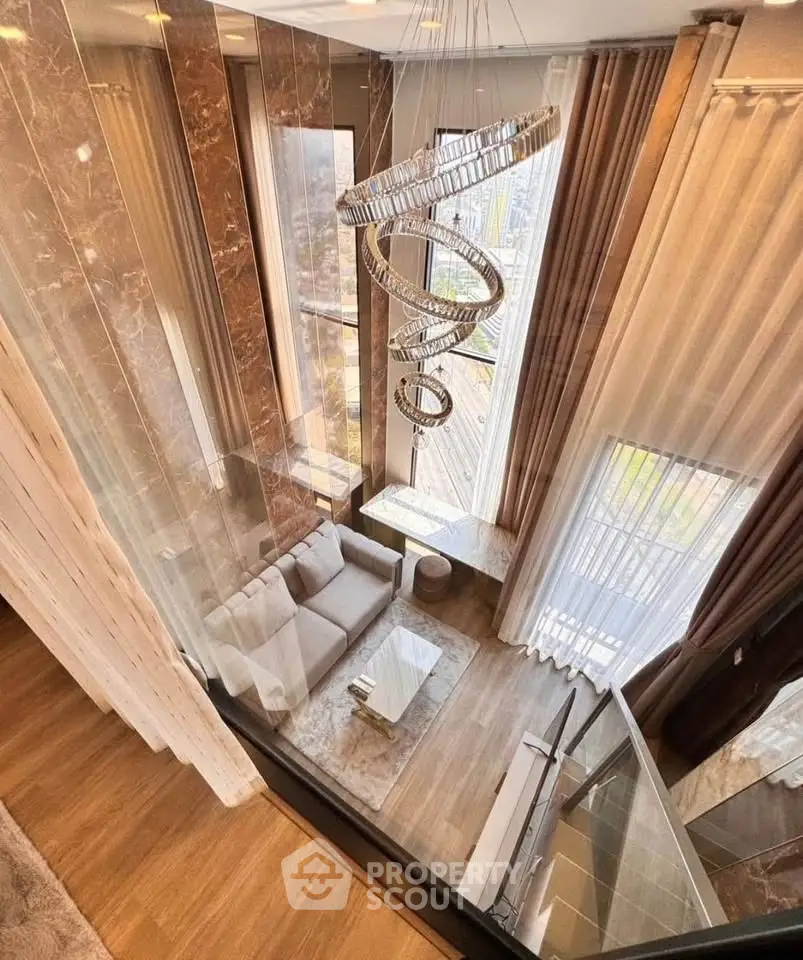 Luxurious high-ceiling living room with modern chandelier and floor-to-ceiling windows.