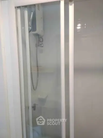Compact bathroom shower with sliding glass door and modern fixtures.