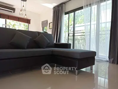 Modern living room with sleek gray sofa and large windows offering natural light and garden view.