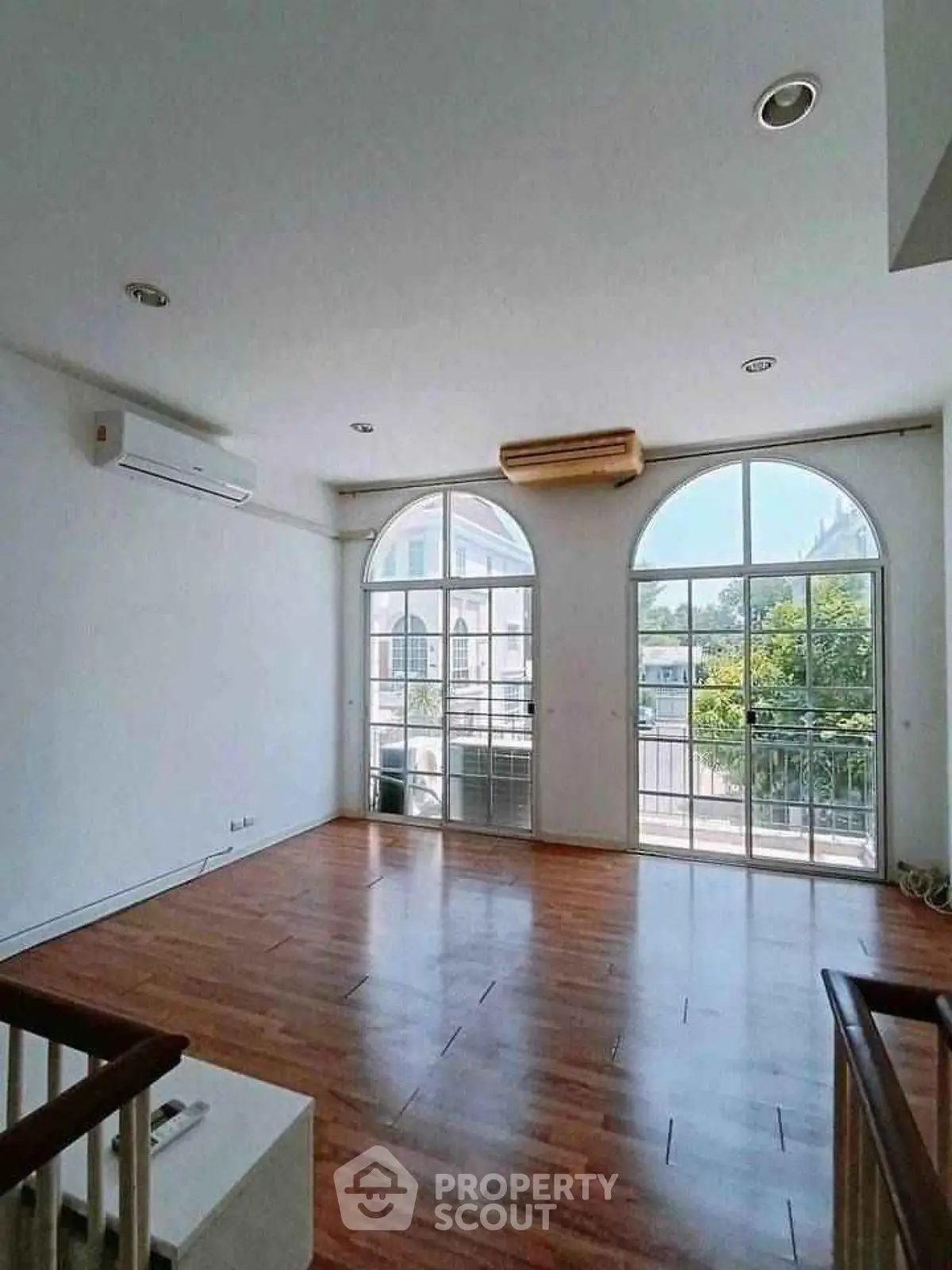 Spacious living room with large windows and wooden flooring, offering abundant natural light.
