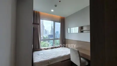Cozy bedroom with city view, featuring a comfortable bed and study desk, perfect for urban living.