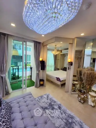 Luxurious bedroom with elegant chandelier and mirrored walls, featuring a cozy seating area and balcony access.