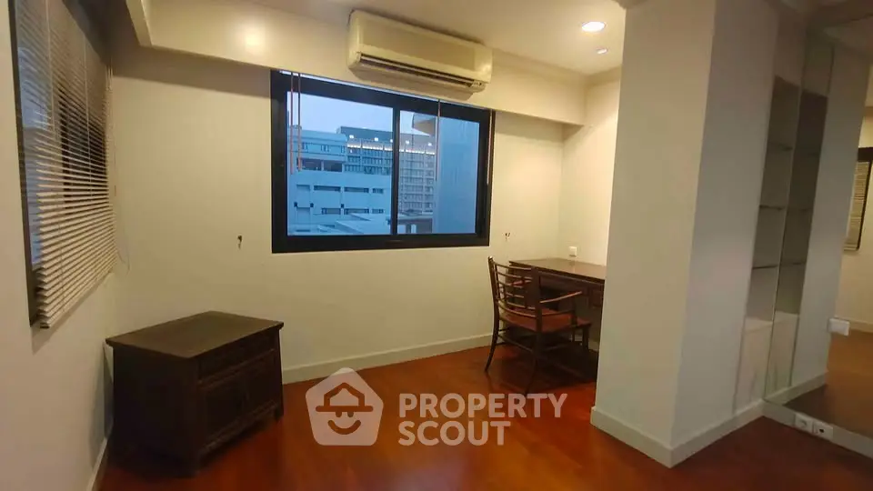 Spacious study room with wooden flooring and large window offering city views.