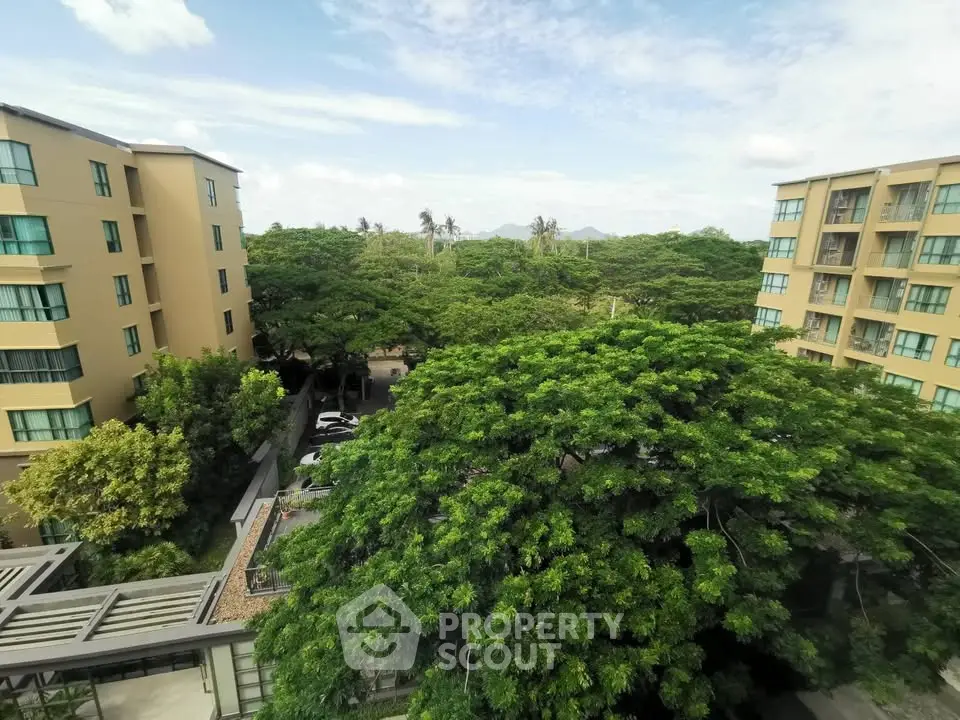 Scenic view from apartment balcony overlooking lush greenery and modern buildings.