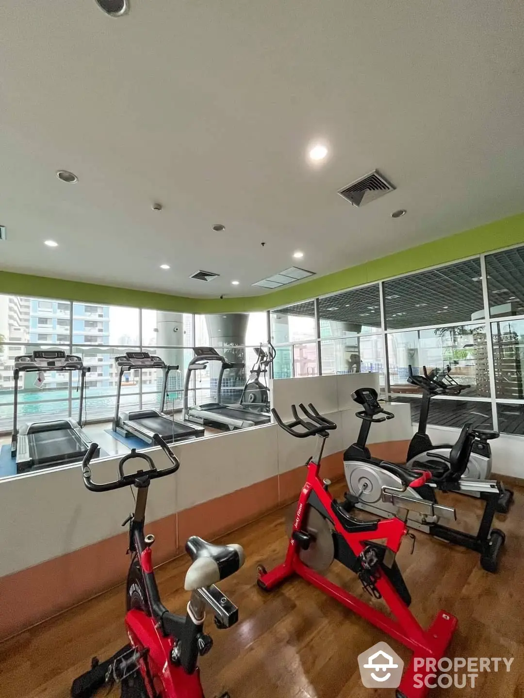 Modern gym facility in a residential building with state-of-the-art exercise bikes and treadmills, natural light, and a view of the city, perfect for fitness enthusiasts.