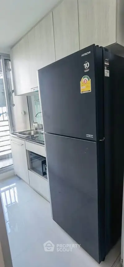 Modern kitchen with sleek black fridge and built-in appliances in a compact layout.