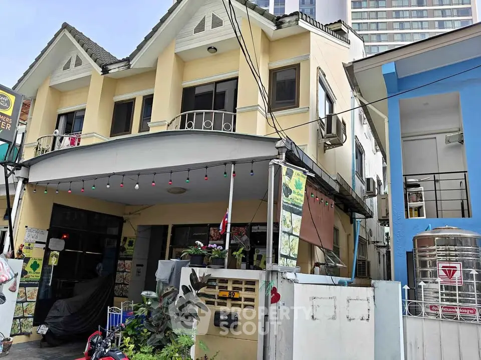 Charming two-story yellow house with decorative balcony and festive lights, perfect for urban living.