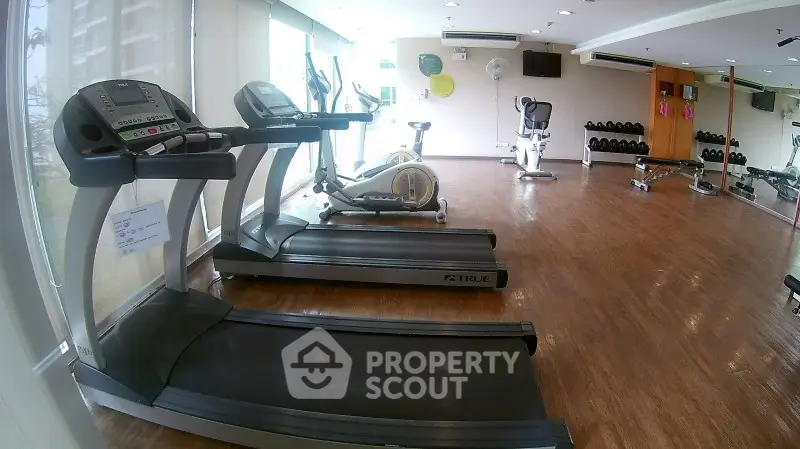 Spacious gym with modern equipment and wooden flooring in a residential building.