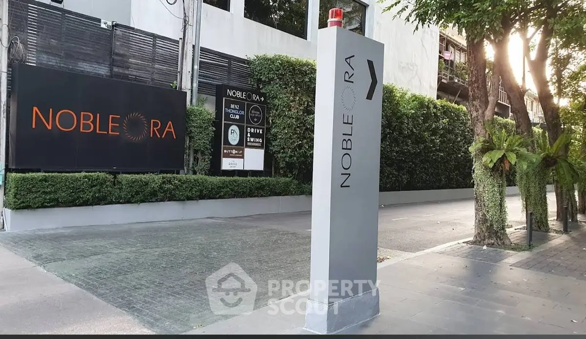 Modern entrance of Noble Ora with lush greenery and sleek signage.