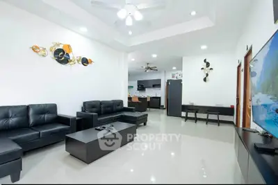 Spacious modern living room with sleek black furniture and open layout to kitchen area.