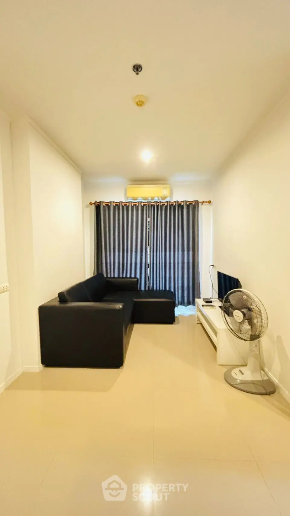 Modern living room with sleek black sofa, TV, and fan, featuring floor-to-ceiling curtains and air conditioning.