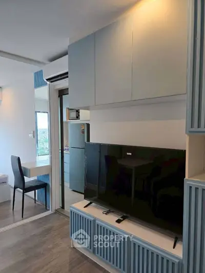 Modern living room with sleek cabinetry and large TV, open layout to kitchen.