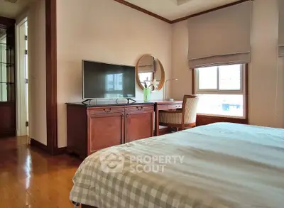 Cozy bedroom with wooden furniture and natural light, featuring a TV and a stylish round mirror.