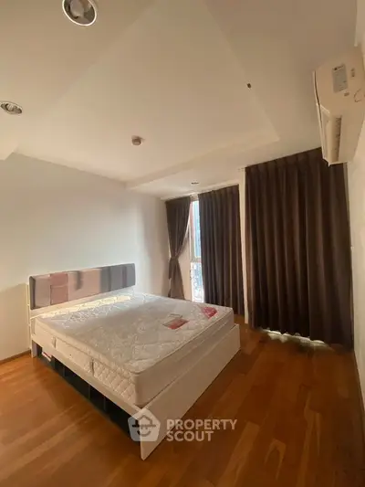 Spacious bedroom with wooden flooring and natural light