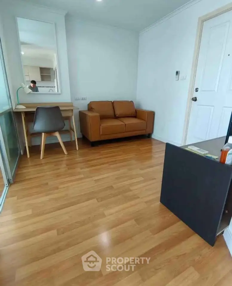 Cozy living room with wooden flooring, brown sofa, and modern desk setup.