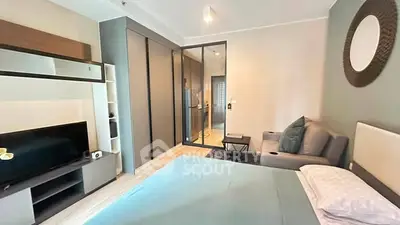 Modern bedroom with stylish decor and glass partition leading to a sleek kitchen area.