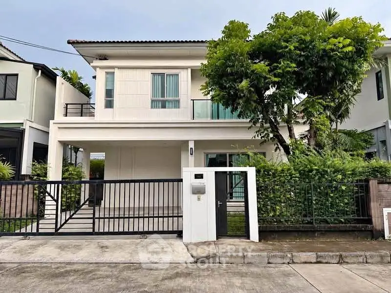 Modern two-story house with gated entrance and lush greenery in a serene neighborhood.