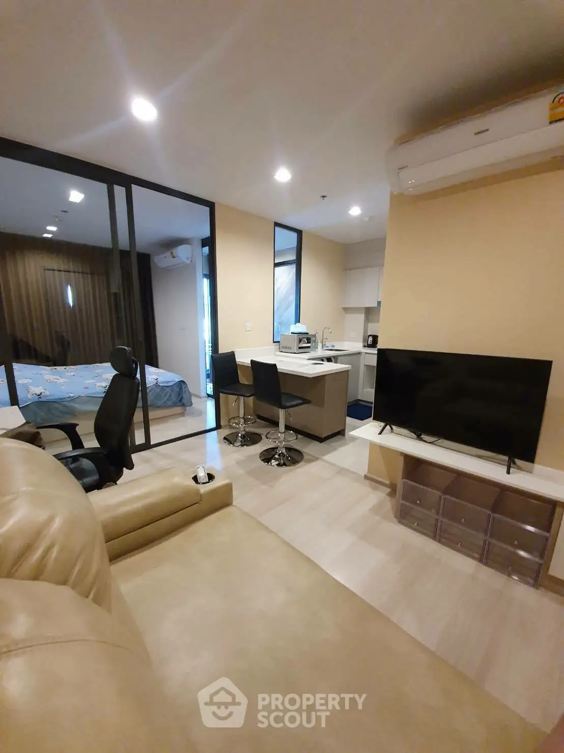 Modern open-plan living room with kitchen and bedroom view, featuring sleek furniture and neutral tones.