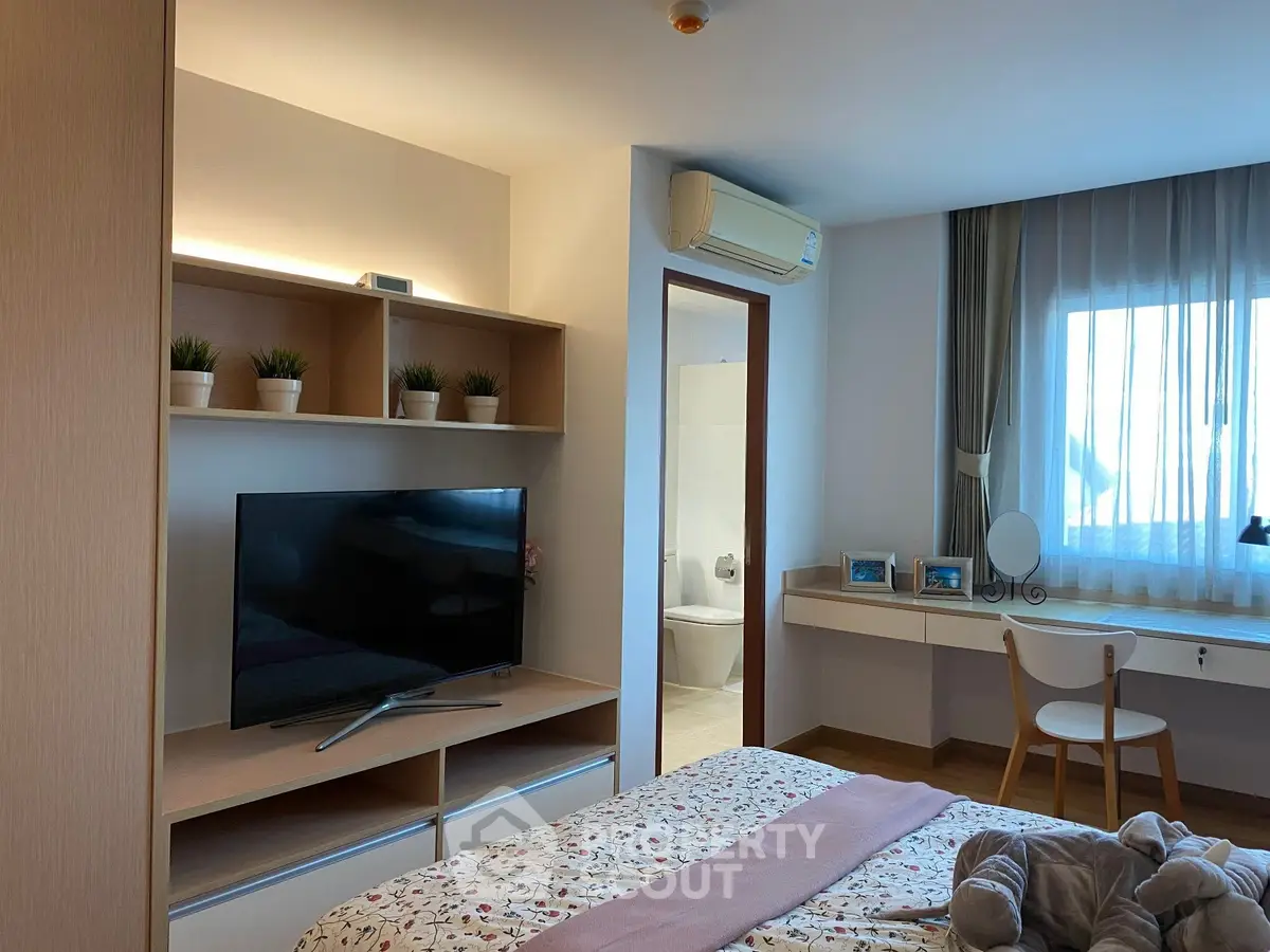 Cozy bedroom with modern decor, featuring a TV, air conditioning, and a window with natural light.