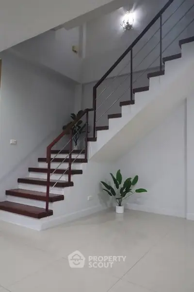 Elegant staircase with modern railing and potted plants in a minimalist home interior.