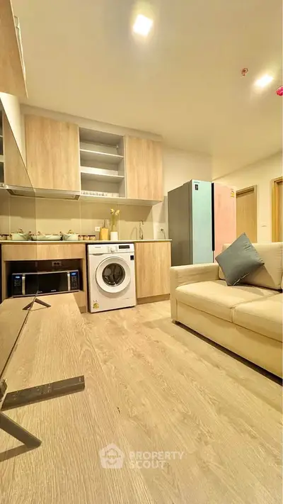 Modern living room with integrated kitchen and washing machine, featuring sleek wooden cabinetry.