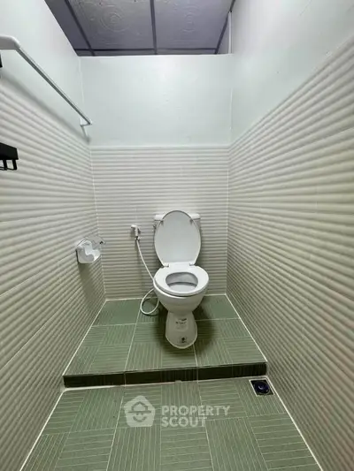 Minimalist bathroom with elevated toilet and green tiled flooring