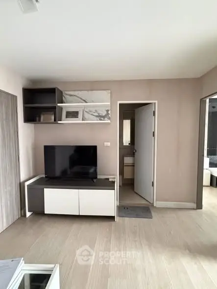 Modern living room with sleek TV stand and open doorway to bathroom, featuring light wood flooring.