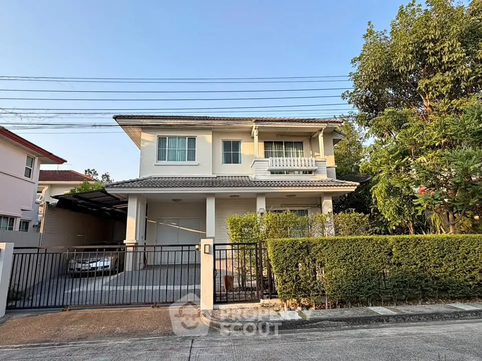 Charming two-story house with gated driveway and lush greenery, perfect for family living.