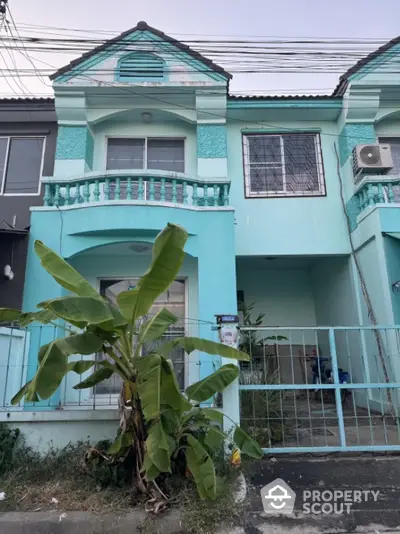 Charming turquoise townhouse with balcony and lush greenery in front yard