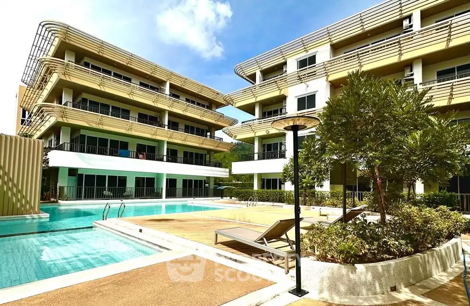 Luxurious modern apartment complex with pool and sun loungers under a clear blue sky.