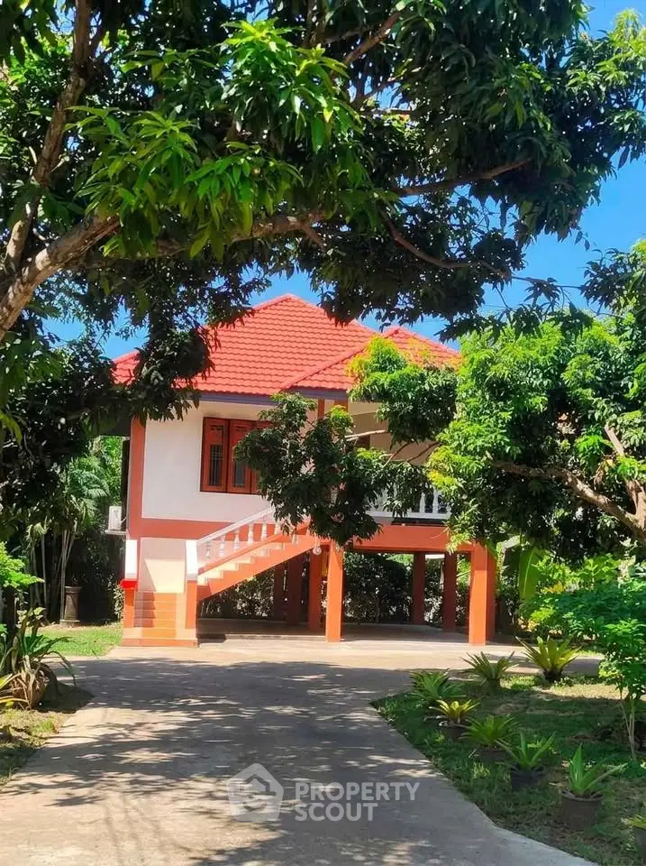 Charming elevated house with red roof surrounded by lush greenery and trees, offering serene outdoor living.