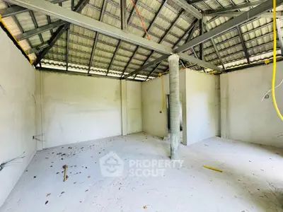 Spacious unfinished room with high ceiling and exposed beams, ideal for customization.