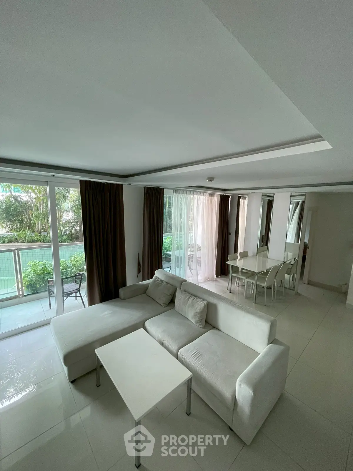 Spacious living room with modern white sofa and dining area, featuring large windows and garden view.