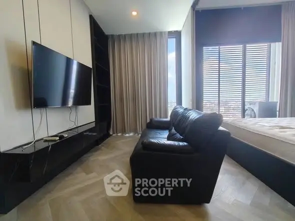 Modern living room with sleek black sofa and wall-mounted TV, featuring large windows with city view.
