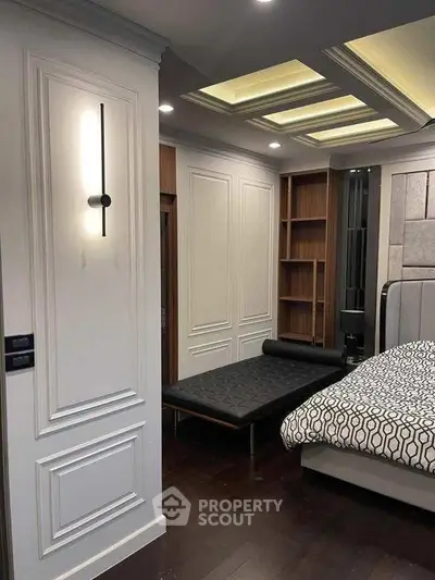 Luxurious bedroom with elegant paneling and modern lighting, featuring a stylish bed and chaise lounge.