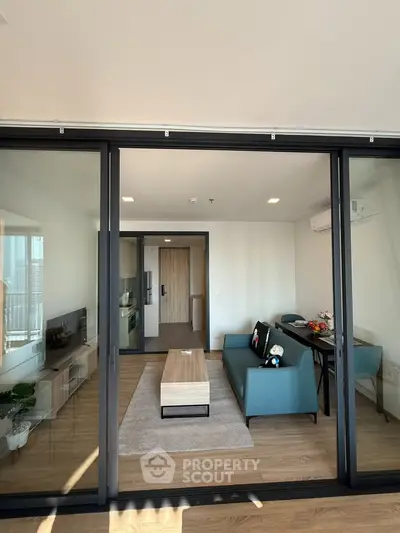 Modern living room with sleek design and large glass doors opening to a balcony, featuring stylish furniture and decor.