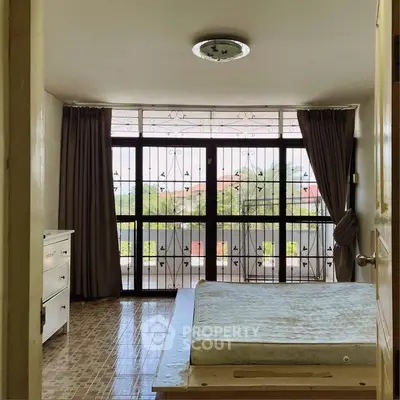 Spacious bedroom with large window and balcony view, featuring elegant curtains and ample natural light.