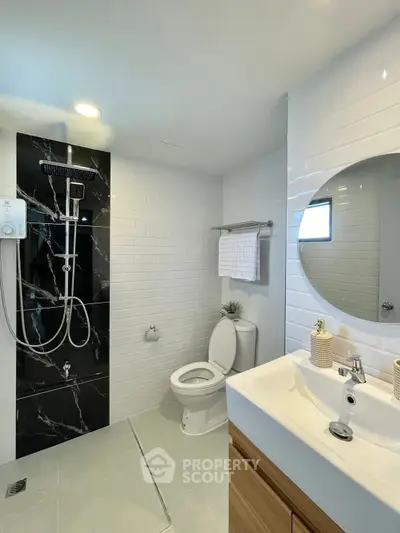 Modern bathroom with sleek black shower panel and white tiles, featuring a round mirror and stylish fixtures.