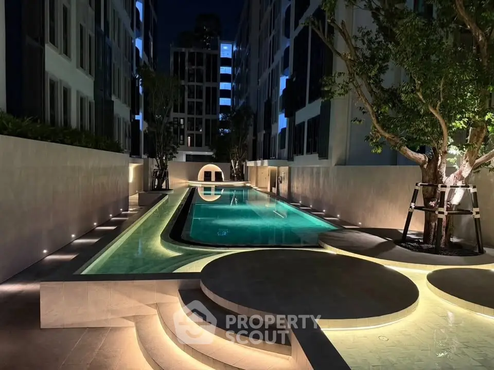 Luxurious modern apartment complex with illuminated outdoor pool at night, surrounded by sleek architecture.