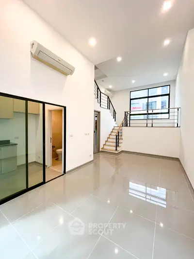 Spacious modern living room with high ceilings and mezzanine, featuring sleek tile flooring and large windows.