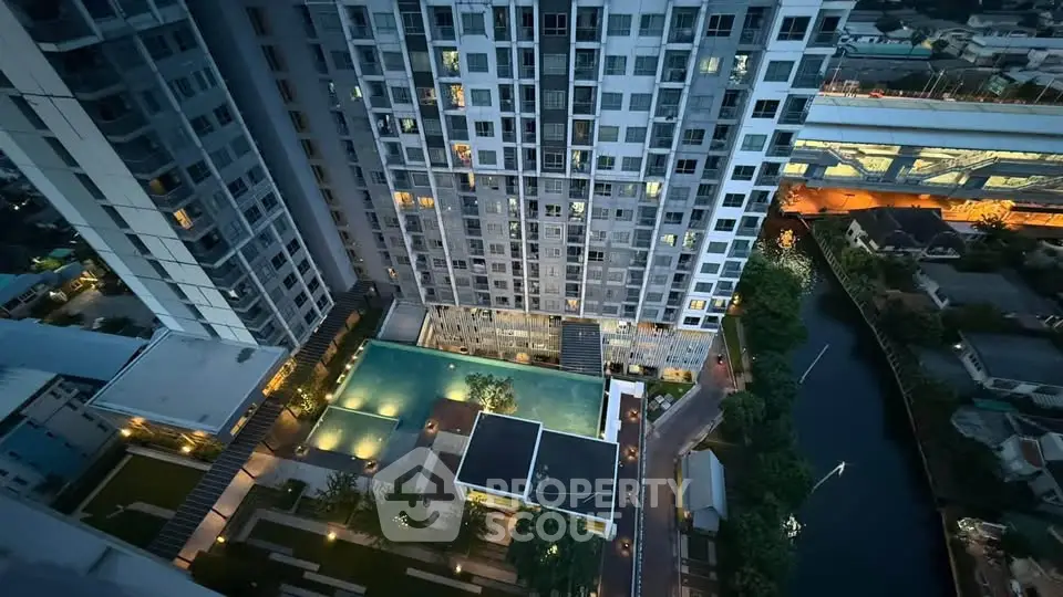 Stunning aerial view of modern high-rise building with illuminated pool and lush surroundings.