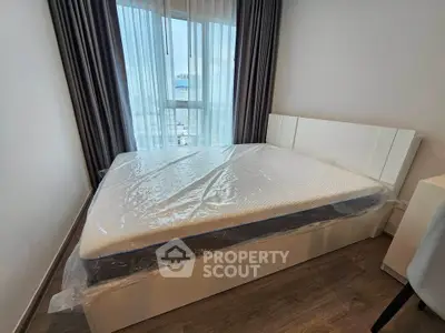 Modern bedroom with large window and city view, featuring a new mattress and stylish decor.