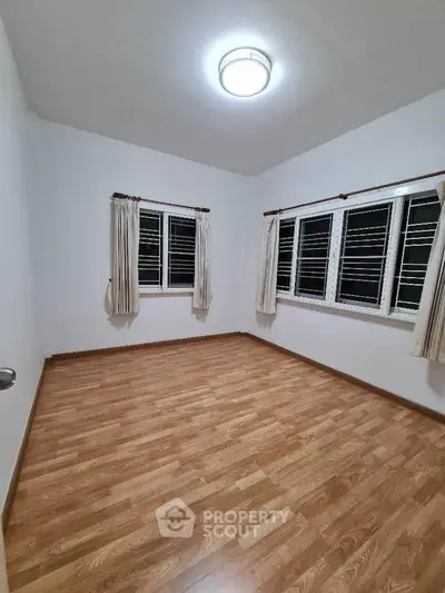Spacious empty bedroom with wooden flooring and large windows for natural light.