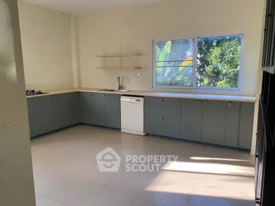 Spacious kitchen with modern cabinets and large window overlooking lush greenery.