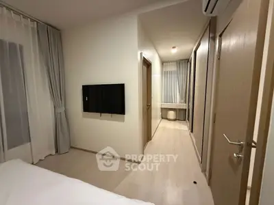 Modern bedroom with minimalist decor and wall-mounted TV, featuring light wood flooring and soft lighting.