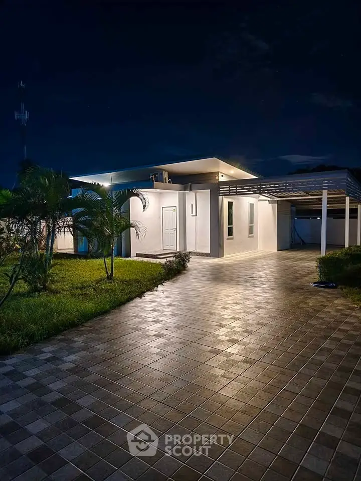 Stunning modern home exterior with sleek driveway and lush landscaping at night.